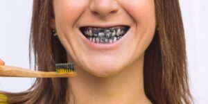 Woman brushing teeth with charcoal toothpaste, showing black-stained smile.