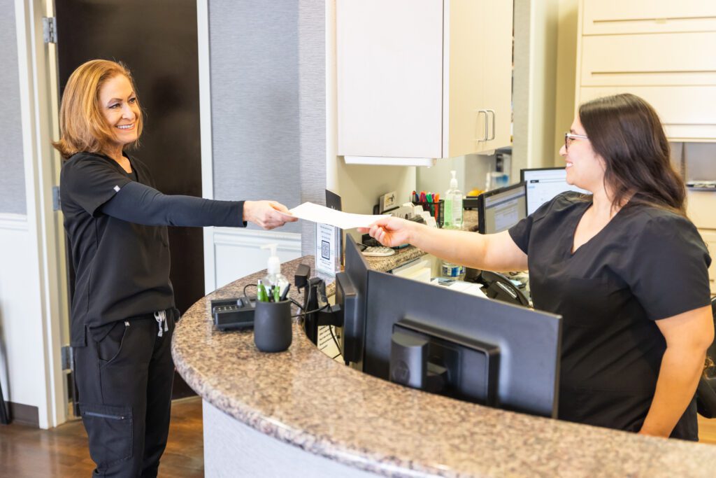 Dental office staff members exchanging paperwork at the reception counter inside a dental clinic.